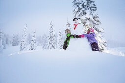 Children embracing a snowman, Passo Monte Croce di Comelico, South Tyrol, Italy