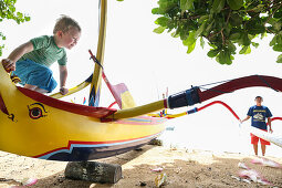 Young boy climbing on boat, traditional fisherboat, 3 years old, beach, eye, colorful boat, prahu, play, family travel, Indian Ocean, parental leave, MR, Sanur, Bali, Indonesia