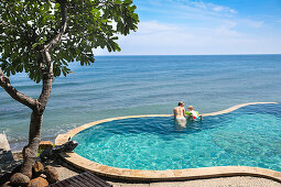 Mother and son in a swimming pool, overflow pool, infinity pool, looking to the sea, happiness, sea, tree, blue sky, paradise, luxury, family travel in Asia, parental leave, German, European, MR, Amed, Bali, Indonesia