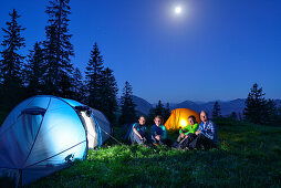 Four persons sitting in front of two illuminated tents, Blauberge, Bavarian Prealps, Upper Bavaria, Bavaria, Germany