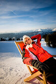 Junge Frau im Liegestuhl sonnt sich im Schnee, Kreischberg, Murau, Steiermark, Österreich