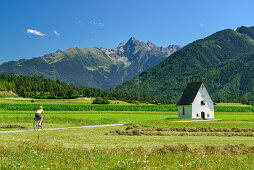 Woman cycling along Inn cycle route, chapel and Oetztal Alps in background, Karres, Tyrol, Austria
