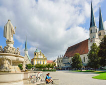 Cyclist resting at Marienbrunnen fountain, Kapellplatz, Altoetting, Upper Bavaria, Germany