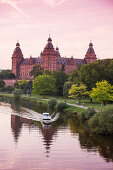 Schloss Johannisburg und Parklandschaft am Ufer vom Fluss Main mit Mainradweg und Motorboot auf Fluss bei Sonnenuntergang, Aschaffenburg, Franken, Bayern, Deutschland