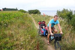 Fahrradfahrer mit Kinderanhänger fährt Küstenweg entlang, Marielyst, Falster, Dänemark