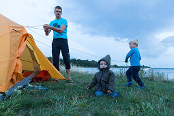 Father and children (1-4 years) putting up a tent, Guldborg, Falster, Denmark