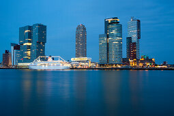 Cruise ship MS Deutschland (Reederei Peter Deilmann) at Rotterdam Cruise Terminal on Nieuwe Maas river with high-rise buildings of Kop van Zuid area and Erasmus Bridge at dusk, Rotterdam, South Holland, Netherlands