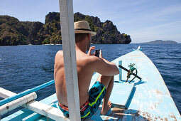 Junger Mann mit Handy auf einem Boot im Bacuit-Archipel vor El Nido, Insel Palawan im Südchinesischen Meer, Philippinen, Asien