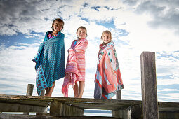 Three girls wrapped in towels on a jetty at lake Starnberg, Upper Bavaria, Bavaria, Germany