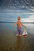 Junge mit einem Spielzeugsegelboot steht im Starnberger See, Oberbayern, Bayern, Deutschland