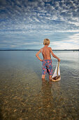 Boy with toy sail boat standing in lake Starnberg, Upper Bavaria, Bavaria, Germany