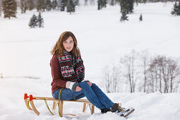 Young woman sitting on a sled, Spitzingsee, Upper Bavaria, Germany