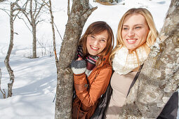 Zwei junge Frauen zwischen Baumstämmen, Spitzingsee, Oberbayern, Bayern, Deutschland