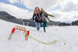 Zwei junge Frauen rennen durch den Schnee, Spitzingsee, Oberbayern, Bayern, Deutschland