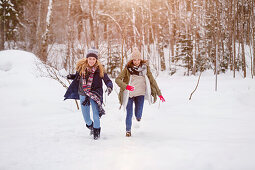 Zwei junge Frauen rennen im Schnee, Spitzingsee, Oberbayern, Bayern, Deutschland