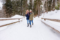 Two young women walking in snow, Spitzingsee, Upper Bavaria, Germany