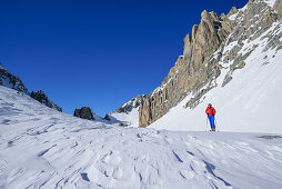 Woman back-country skiing standing beneath rock wall of Monte Sautron, Valle Maira, Cottian Alps, Piedmont, Italy