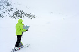 Frau auf Skitour blickt bei Schlechtwetter auf Landkarte, Serriera di Pignal, Valle Stura, Cottische Alpen, Piemont, Italien