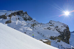 Frau auf Skitour steigt an Almhütte vorbei zum Monte Salza auf, im Hintergrund Rocca Senghi, Monte Salza, Valle Varaita, Cottische Alpen, Piemont, Italien