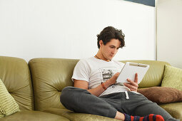 Young man sitting on the sofa, playing with his tablet