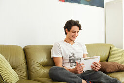 Junger Mann sitzt auf dem Sofa und spielt auf dem Tablet