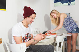 Junges Paar in der Küche, spielt mit Handy und frisst Pizza