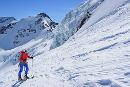Woman back-country skiing ascending towards Punta San Matteo, Punta Cadini and icefall in background, Punta San Matteo, Val dei Forni, Ortler range, Lombardy, Italy