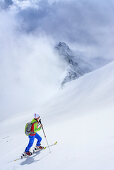 Woman back-country skiing ascending through clouds towards Grundschartner, Grundschartner, Zillergrund, Zillertal Alps, Tyrol, Austria