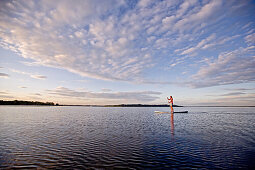 Woman stand up paddling on lake Chiemsee in sunset, Chiemgau, Bavaria, Germany