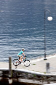 Junge Frau fährt mit ihren Fahrrad am Hafen an einem See, Gardasee, Italien