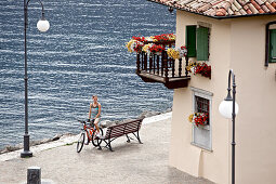 Young woman having a break with her bike at a bench near a lake, Lake Garda, Italy