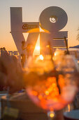 Love sculpture on the beach seen through a cocktail glass at sunset, Ostend, Flanders, Flemish Region, Belgium