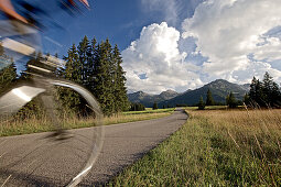 Junge Frau fährt Fahrrad in der Nähe der Berge an einem sonnigen Tag, Tannheimer Tal, Tirol, Österreich