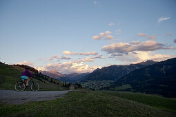 Junge Frau fährt mit ihrem Fahrrad in der Nähe der Berge bei Sonnenuntergang, Rote Flüh, Gimpel, Hochwiesler, Tannheimer Tal, Tirol, Österreich