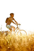 Young woman riding her bike near a meadow on a sunny day, Tannheimer Tal, Tyrol, Austria