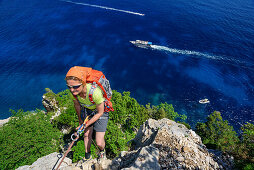 Woman rapelling over rockface, Mediterranean in background, Selvaggio Blu, National Park of the Bay of Orosei and Gennargentu, Sardinia, Italy