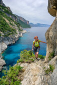 Woman hiking Selvaggio Blu over rock ledge with view to bay, Selvaggio Blu, National Park of the Bay of Orosei and Gennargentu, Sardinia, Italy