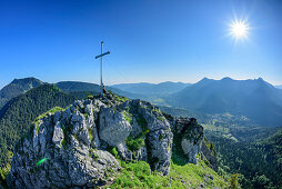 Person sitzt am Gipfelkreuz des Leonhardstein, Blick auf Tegernseer Berge, Leonhardstein, Bayerische Alpen, Oberbayern, Bayern, Deutschland