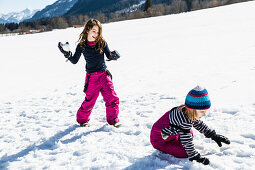 Mädchen schmeißt Schneeball auf Jungen bei einer Schneeballschlacht im Winter, Pfronten, Allgäu, Bayern, Deutschland