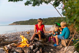Mother and children eating corn on the cob around the campfire, Adventure, Baltic sea, MR, Bornholm, near Gudhjem, Denmark, Europe