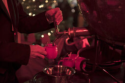 Auf einem Weihnachtsmarkt füllt ein Barkeeper eine Tasse mit Feuerzangenbowle aus dem Kessel ab,  Berlin, Deutschland 2015