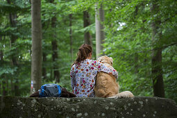 Young woman and Golden Retriever dog sit atop Lange Steine rock formation in Hessisches Kegelspiel mountains