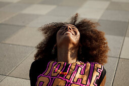Young afro-american woman sitting relaxed and laughing on a graphical floor, Lenbachplatz, Munich, Bavaria, Germany