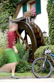 Junge Frau läuft zu ihrem Fahrrad an einem alten Wasserrad
