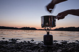 Person kocht mit einem Campingkocher an einem See bei Nacht, Freilassing, Bayern, Deutschland