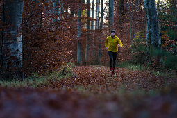 Young man running on a trail through a forest, Allgaeu, Bavaria, Germany