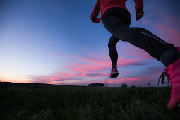 Young woman running over a field at sunset, Allgaeu, Bavaria, Germany