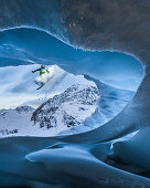 Young male snowboarder jumping down from a cave of a glacier, Pitztal, Tyrol, Austria