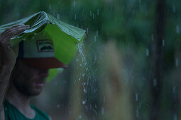 Junge Mann hält ein großes Blatt über seinen Kopf um sich vor dem Regen zu schützen, Sao Tome, Sao Tome und Príncipe, Afrika