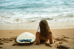 Junge Surferin sitzt am Strand mit ihrem Surfbrett, Sao Tome, Sao Tome und Príncipe, Afrika